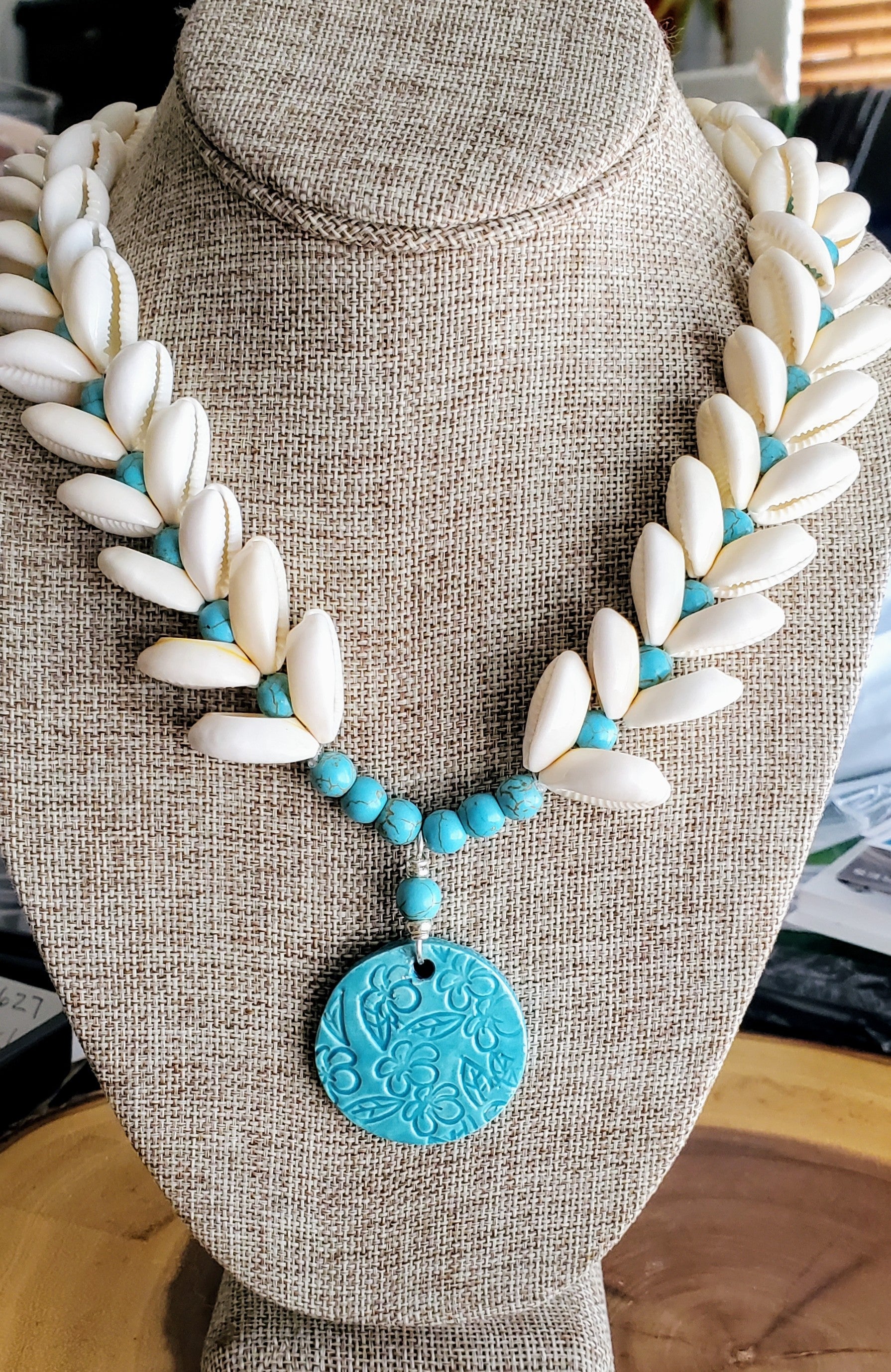 Handcrafted Ceramic necklace with Plumeria design on the pendant, glazed with Aqua glaze, hand-strung with Cowrie Shells and Turquoise Beads necklace.
